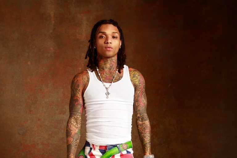 American rapper and singer Swae Lee posing in a white tank top with visible tattoos.